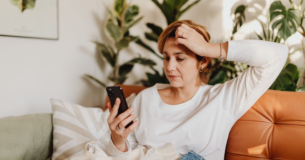 Compradora mirando el celular con cara de duda antes de terminar una compra: un carrito abandonado a punto de pasar