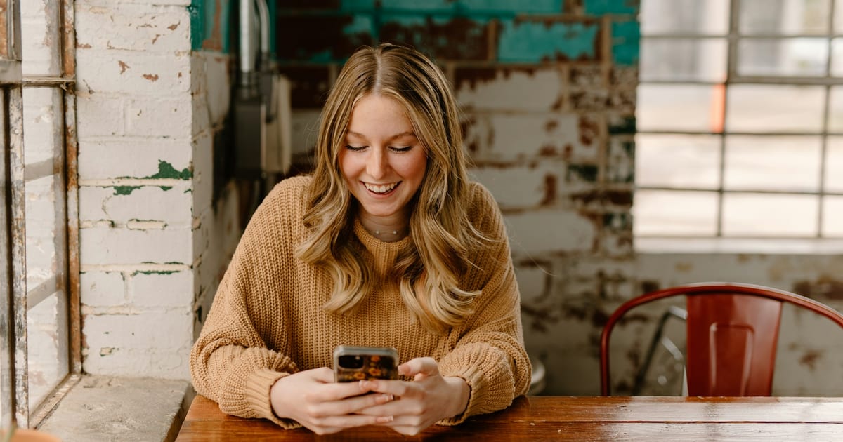 Persona sonriendo mientras mira en el celular el catálogo digital de una tienda