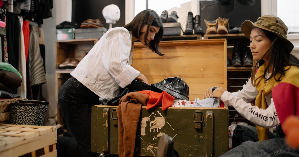Dos personas revisando prendas de ropa usada en un baúl dentro de un local de segunda mano